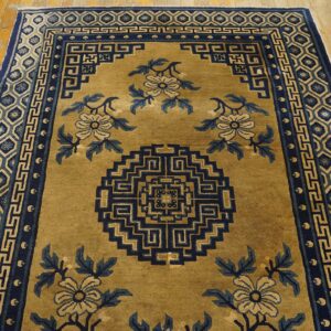 Low-pile goldenrod rug with blue floral and geometric patterns resting on light wooden floorboards.