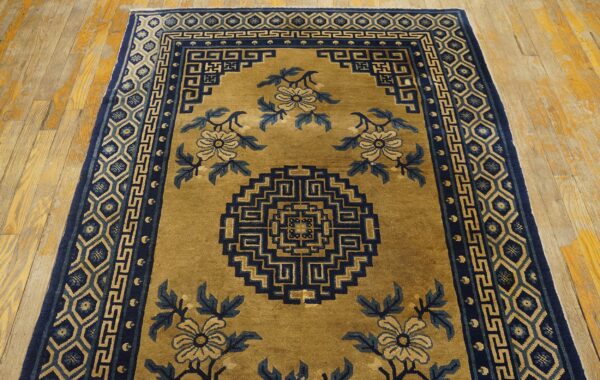 Low-pile goldenrod rug with blue floral and geometric patterns resting on light wooden floorboards.