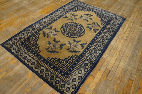 A low-pile rug in gold and navy blue with geometric and floral patterns on worn wood planks.