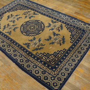 Tan field rug with deep blue geometric borders and floral designs rests on distressed wood flooring.