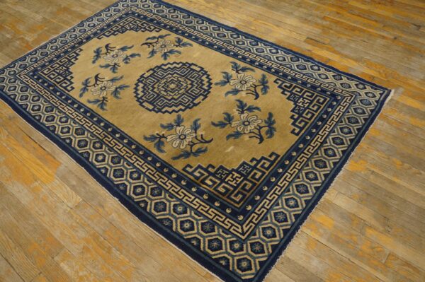 Tan field rug with deep blue geometric borders and floral designs rests on distressed wood flooring.
