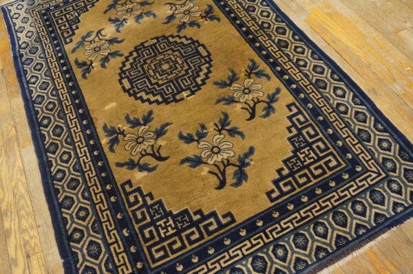 Low-pile gold rug with navy blue geometric borders and large floral motifs on light wood flooring.