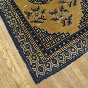 Gold rug with navy blue geometric borders and floral motifs lying on rustic wood floor.