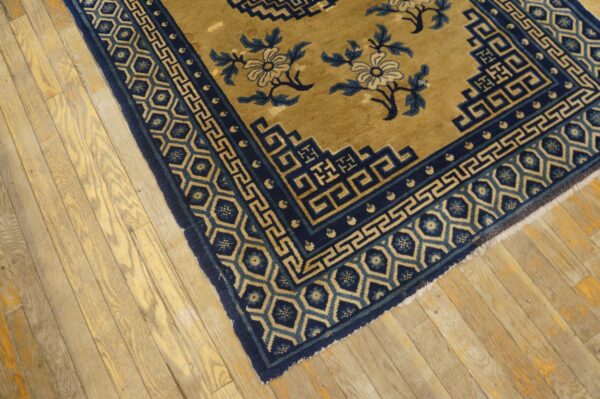 Gold rug with navy blue geometric borders and floral motifs lying on rustic wood floor.