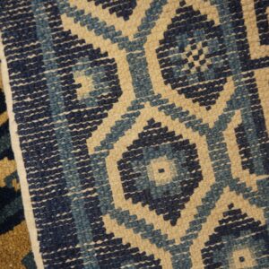 A low-pile rug displaying a stepped diamond lattice pattern in navy, light blue, and beige colors.