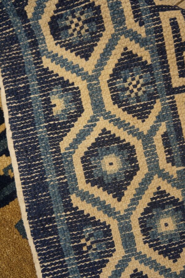 A low-pile rug displaying a stepped diamond lattice pattern in navy, light blue, and beige colors.
