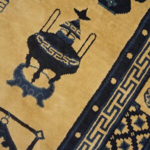 Golden yellow and navy blue plush rug displaying an urn motif and geometric meander border design.