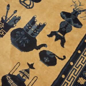 A velvety, tan-field rug displaying dark blue stylized objects and a detailed Greek key border.