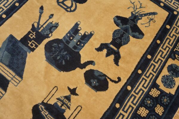 A velvety, tan-field rug displaying dark blue stylized objects and a detailed greek key border.