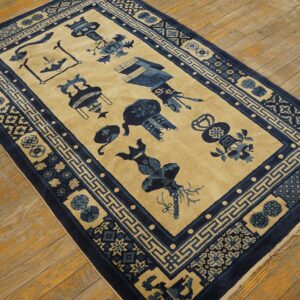 Tan rug with dark blue stylized vessels and geometric borders rests on diagonal wood plank flooring.