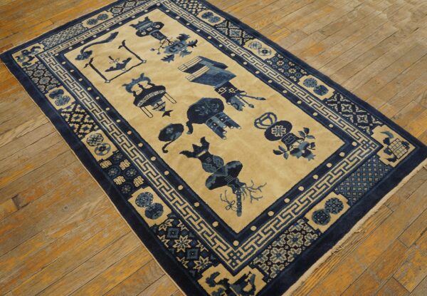 Tan rug with dark blue stylized vessels and geometric borders rests on diagonal wood plank flooring.