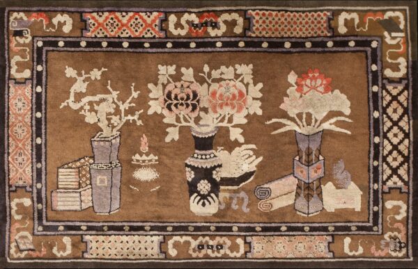 Decorative brown rug depicting pink and cream flowers in vases alongside books and scrolls within a complex border.