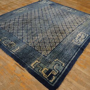Deep blue rug with a light blue geometric lattice and border on distressed rustic hardwood flooring.