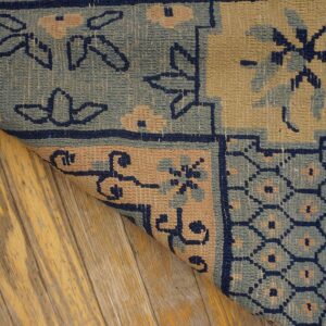 Low-pile rug detail in navy, light blue, and tan shows geometric patterns on distressed yellow wood planks.