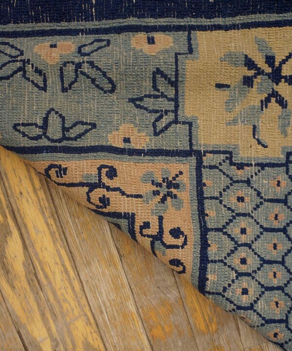 Low-pile rug detail in navy, light blue, and tan shows geometric patterns on distressed yellow wood planks.
