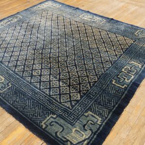 A dark blue rug with a repeating geometric quatrefoil pattern and detailed borders sits on light wood flooring.