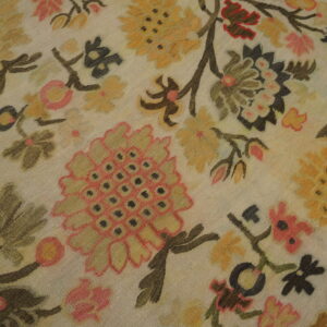Detailed low-pile rug with stylized cream, gold, pink, and deep brown large floral patterns on wood flooring.
