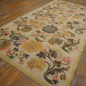 Cream rug with rambling pink, yellow, and brown floral pattern and a thin border, resting on hardwood flooring.
