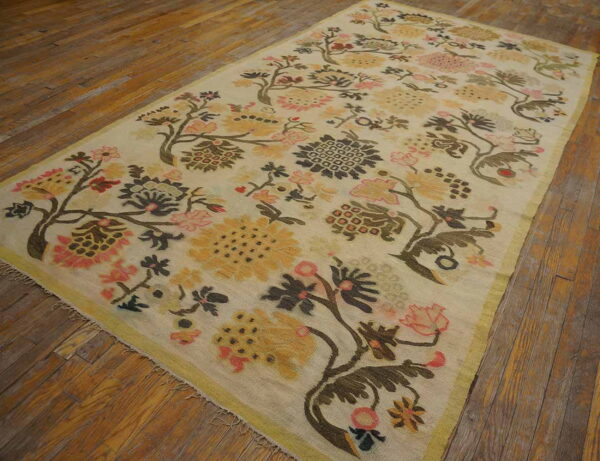 Cream rug with rambling pink, yellow, and brown floral pattern and a thin border, resting on hardwood flooring.