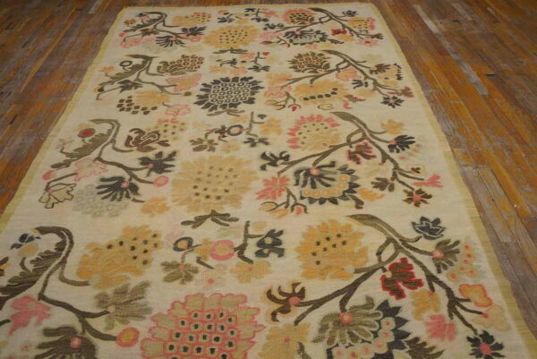 Ivory rug with sprawling floral vines in muted pink, gold, and charcoal on rustic wood floors.