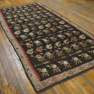 Dark flatweave runner rug with repeating cream, red, and olive floral motifs laid on a wood floor.
