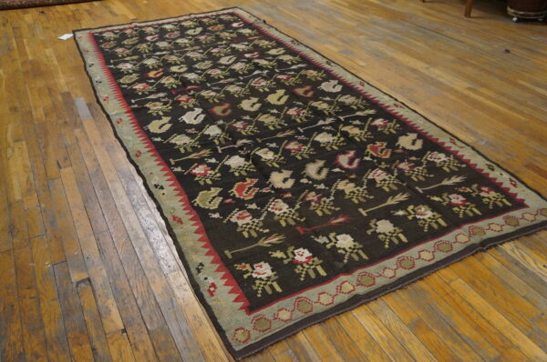 Dark flatweave runner rug with repeating cream, red, and olive floral motifs laid on a wood floor.