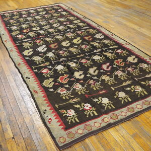 A flatweave runner with brown, red, and beige repeating patterns lies on rustic wooden flooring.