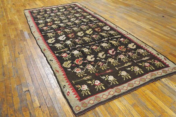 A flatweave runner with brown, red, and beige repeating patterns lies on rustic wooden flooring.