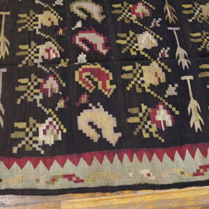 Dark flatweave rug displaying repeating abstract floral and arrow motifs in red, cream, and olive green.