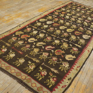 Dark brown flatweave rug featuring repetitive red, beige, and sage motifs rests on distressed wooden floorboards.