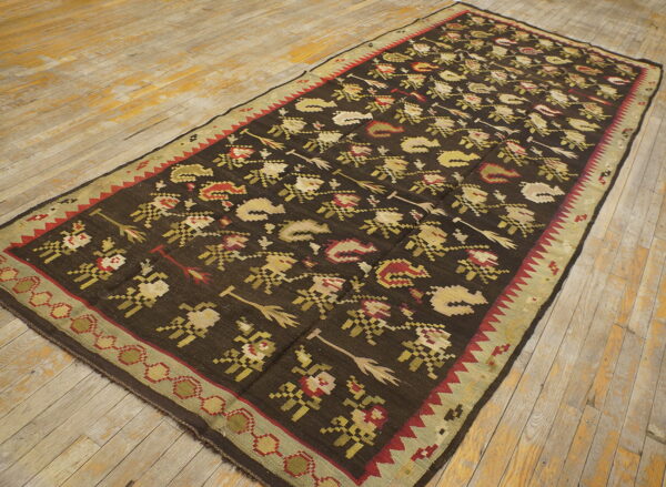 Dark brown flatweave rug featuring repetitive red, beige, and sage motifs rests on distressed wooden floorboards.