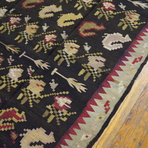 Flat-woven rug with geometric red, cream, and olive patterns on a black field and a plank wood floor.