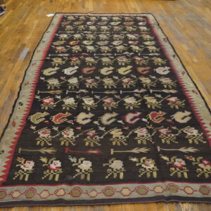 Dark brown flatwoven runner with repeating geometric figures in red, sage, and tan on light wood floors.