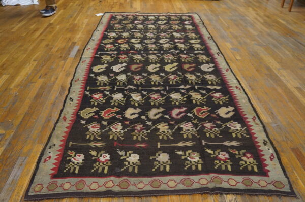 Dark brown flatwoven runner with repeating geometric figures in red, sage, and tan on light wood floors.