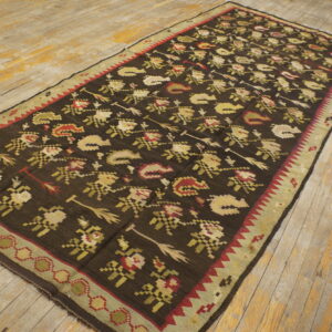 Dark, patterned rug with red and gold motifs and a green border resting on distressed wood flooring.