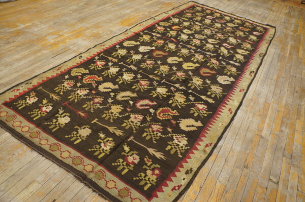 Dark, patterned rug with red and gold motifs and a green border resting on distressed wood flooring.