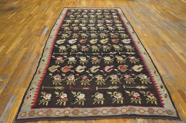 Dark brown runner rug featuring repeating geometric figures and arrows, bordered in olive and red, on wood planks.