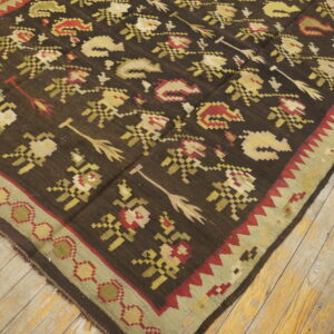 Dark brown flatweave rug featuring stylized floral and arrow motifs on light, rustic wood plank flooring.