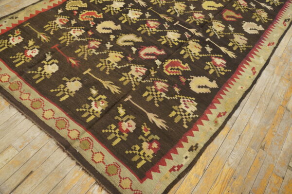 Dark brown flatweave rug featuring stylized floral and arrow motifs on light, rustic wood plank flooring.