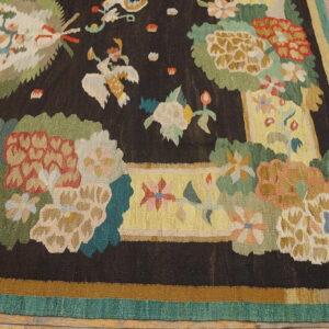 Multicolor floral flatweave rug with a dark field, yellow border, and teal edging on wood planks.