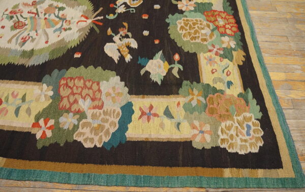 Multicolor floral flatweave rug with a dark field, yellow border, and teal edging on wood planks.