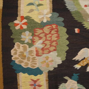 Dark flat-weave rug featuring large, colorful floral and bird patterns, resting on light wood flooring.