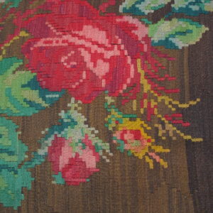 Flatweave rug detail showing stepped red and pink floral motifs on a textured dark brown background.
