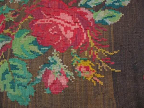 Flatweave rug detail showing stepped red and pink floral motifs on a textured dark brown background.