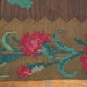 Textured brown flatweave rug with large stepped floral patterns in pink, teal, and shades of green.