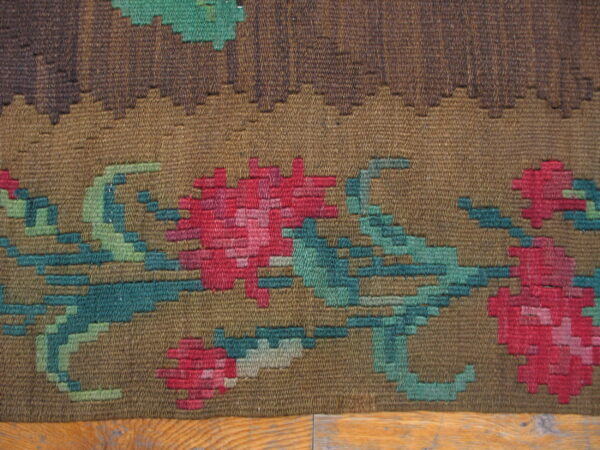 Textured brown flatweave rug with large stepped floral patterns in pink, teal, and shades of green.
