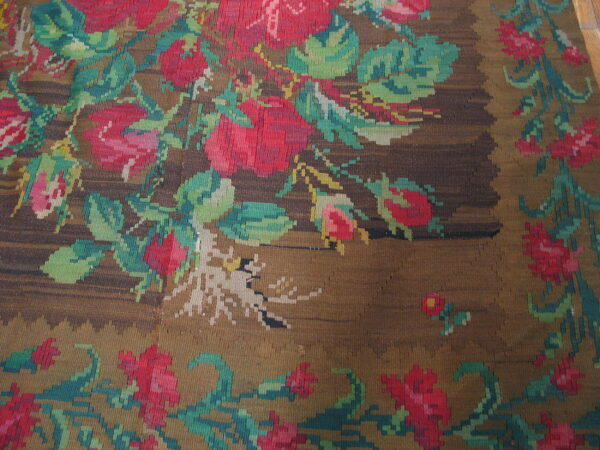 Flatwoven rug featuring red and pink roses and green leaves on a textured brown and gold field.