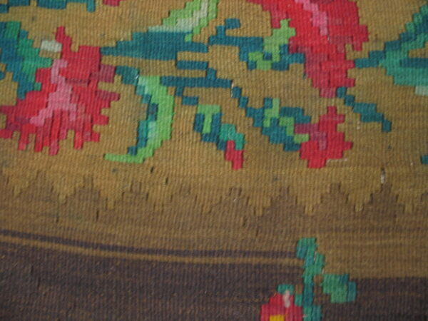 Flatweave rug detail featuring blocky floral designs in red, teal, and green against khaki and dark brown.