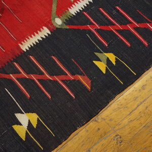 Geometric flatweave rug in red and black with yellow accents resting on distressed hardwood floors.