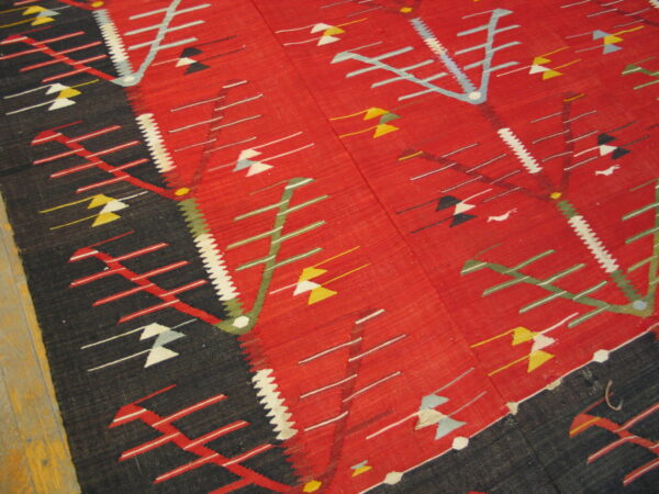 Geometric flatweave rug in red, black, green, and yellow on a wooden floor, seen from an angle.